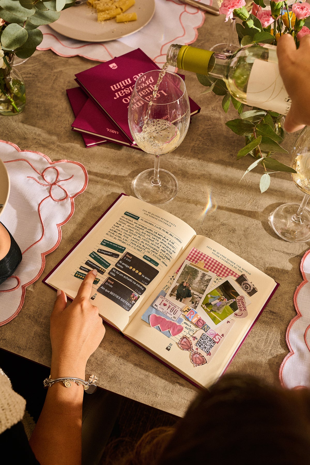 Amigas preenchendo o livro Amiga numa mesa de festa, com a página “Quando quiser ver minhas fotos favoritas de nós” aberta