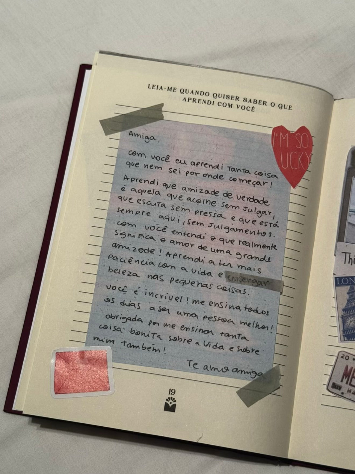 Página 19 do livro Amiga preenchida, “Quando quiser saber o que aprendi com você”: uma carta num papel azul presa com fita e um coração escrito “I’m so lucky”